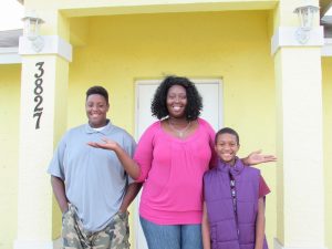 Family of three posing in front of a house